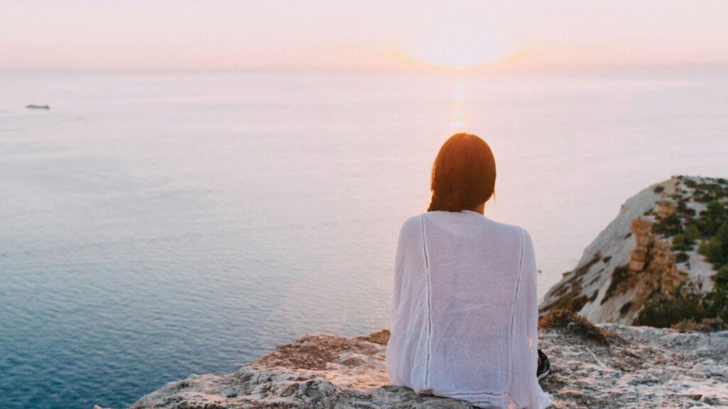 A woman sitting with her back to the camera, gazing at the scenic ocean.